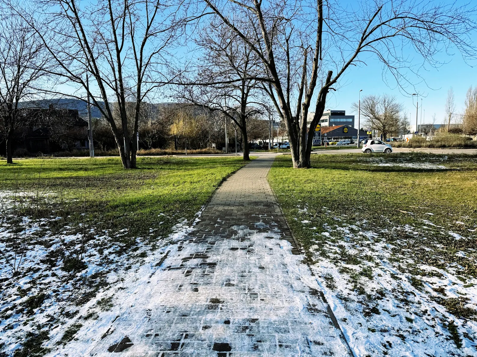 Gångväg och gräsmattor med kvarvarande snö i en Budapestpark